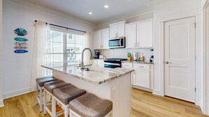 A kitchen with white cabinets, a microwave, a sink, and a bar area with stools. - Brilliant beach house located walking distance to beach with community pool (Orange Beach)