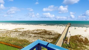 Blick auf einen Strand mit einem Steg, der sich ins Meer erstreckt, feinem Sand und blauem Himmel.