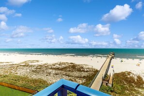 A beach view with a pier extending into the ocean, sandy beach, and clear sky. - Spacious condo with views, pool, beach access, & private fishing pier (Orange Beach)