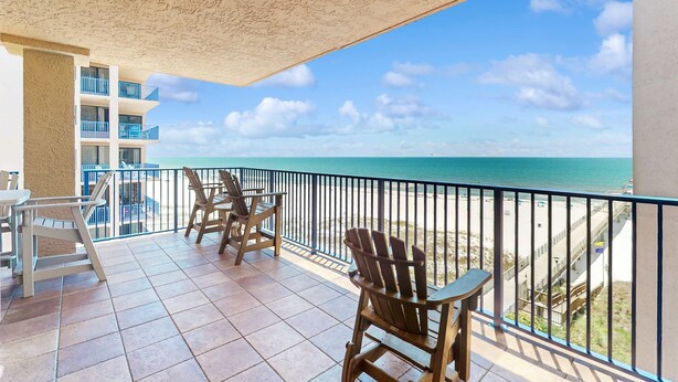 Ein Balkon mit Stühlen und Tisch, mit Blick auf Strand und Meer.