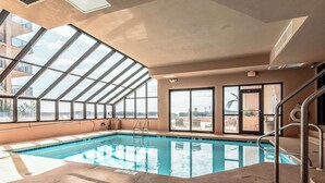 Ein Hallenbad mit Oberlichtern, einer Poolleiter und Blick auf die Stadt durch große Fenster.