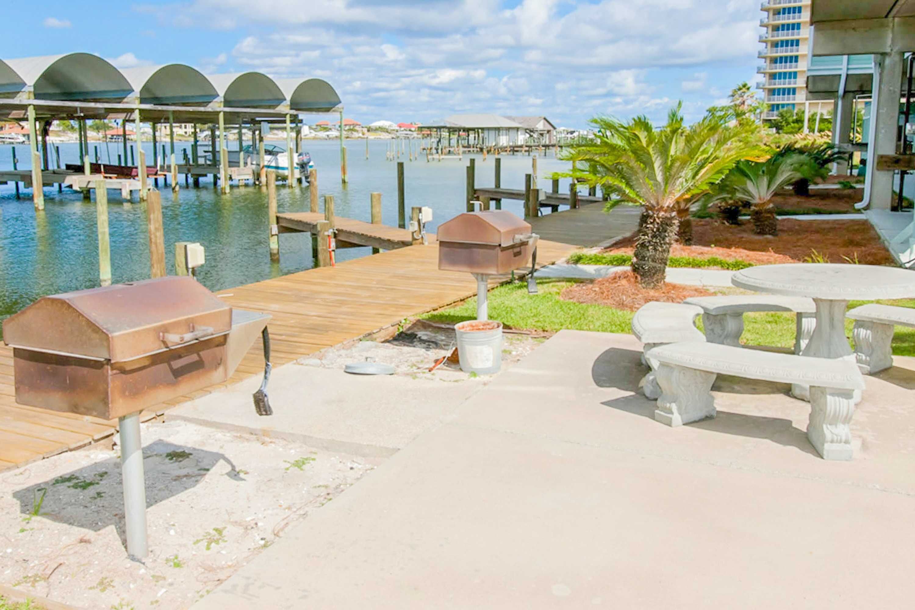 A waterfront patio with barbecue grills, outdoor seating, and a view of the marina.