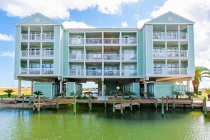 A multi-story hotel with balconies, a dock, and water in front. - Waterfront, gulf view condo by beach with pool, dock & balcony (Orange Beach)