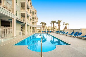 A swimming pool with lounge chairs, a building with balconies, and palm trees. - Gulf view condo with pool & fitness center - balcony, open layout, and W/D (Orange Beach)