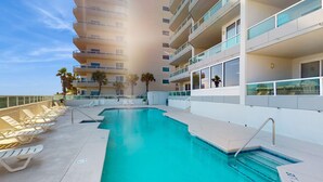 Una piscina en la azotea con tumbonas, cielo despejado y un rascacielos al fondo.