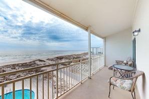 Un balcon avec vue sur la plage, une piscine et du mobilier d’extérieur.