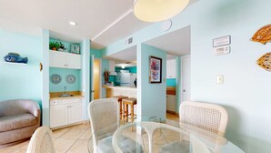 Un salon avec un canapé, une table à manger en verre entourée de chaises, un coin cuisine avec un réfrigérateur et un bar pour prendre les repas.