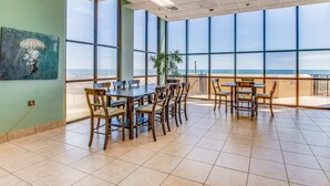 A spacious room with large windows, a dining area with wooden tables and chairs, and a painting on the wall. - Gulf-front fourteenth-floor condo with pools, hot tub & great view (Orange Beach)
