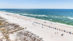 A beach with a long stretch of white sand, a few umbrellas, and a clear view of the ocean. - Gulf-front fourteenth-floor condo with pools, hot tub & great view (Orange Beach)