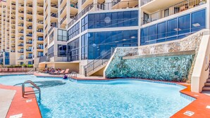 A swimming pool with a stone wall and a multi-story building in the background. - Gulf-front fourteenth-floor condo with pools, hot tub & great view (Orange Beach)