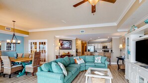 A spacious living room with a sectional sofa, a dining area with wicker chairs, and a kitchen in the background. - Coastal getaway with beach access, pool, hot tub, lazy river, & balcony (Orange Beach)
