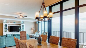 A dining area with wicker chairs, a wooden table, and a chandelier. - Coastal getaway with beach access, pool, hot tub, lazy river, & balcony (Orange Beach)