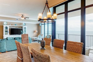 A dining area with wicker chairs, a wooden table, and a chandelier. - Coastal getaway with beach access, pool, hot tub, lazy river, & balcony (Orange Beach)
