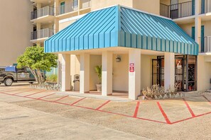 A multi-story building with a blue roofed structure, a parking area with red lines, and a truck parked outside. - Beautiful resort condo at the foot of the beach with pool, WiFi, central AC (Orange Beach)