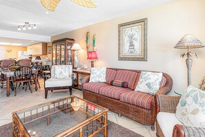 A living room with a sofa, armchairs, a glass coffee table, and a dining area with chairs and a table. - Beautiful resort condo at the foot of the beach with pool, WiFi, central AC (Orange Beach)