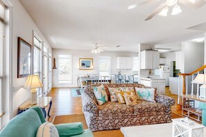A spacious living area with a patterned sofa, a teal armchair, and a dining table with chairs. - Beachy Duplex w/ Full Kitchen, High-Speed WiFi, Central AC, and Washer/Dryer! (Dauphin Island)