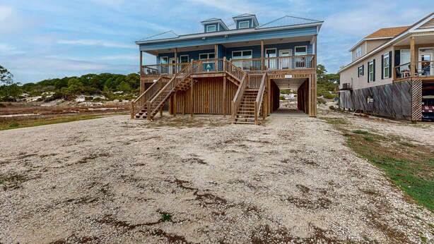 A beachfront property with a large house featuring a wooden deck, a staircase leading to a balcony, and a view of the ocean. - Gulfview duplex with panoramic views, large balcony, and internet (Dauphin Island)