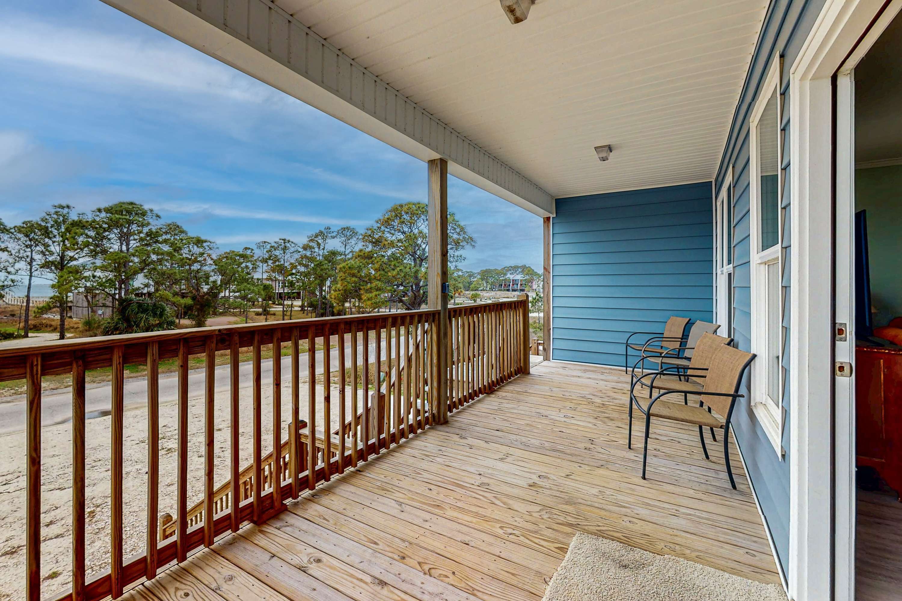 Une terrasse en bois avec une rambarde, un mur extérieur bleu et une porte donnant sur l’intérieur.