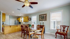 A dining area with a wooden table and chairs, a ceiling fan, and a kitchen with wooden cabinets. - Gulfview duplex with panoramic views, large balcony, and internet (Dauphin Island)