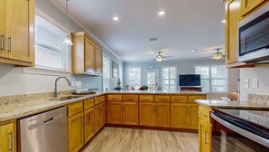 A kitchen with wooden cabinets, a stainless steel dishwasher, granite countertops, and a ceiling fan. - Gulfview duplex with panoramic views, large balcony, and internet (Dauphin Island)