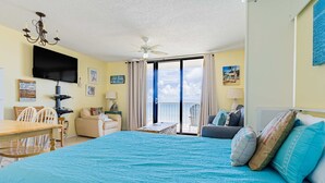 A hotel room with a bed, a desk, a chair, a TV, a ceiling fan, and a balcony with a view. - Seaside escape with balcony, WiFi, pools, tennis, steam room, & gym (Orange Beach)