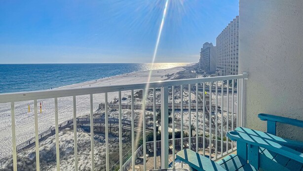 A balcony with a view of a beach, a wooden fence, and a building in the background. - Seaside escape with balcony, WiFi, pools, tennis, steam room, & gym (Orange Beach)