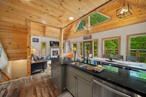 Een moderne keuken met houten balken, een open haard en grote ramen met uitzicht op groen.