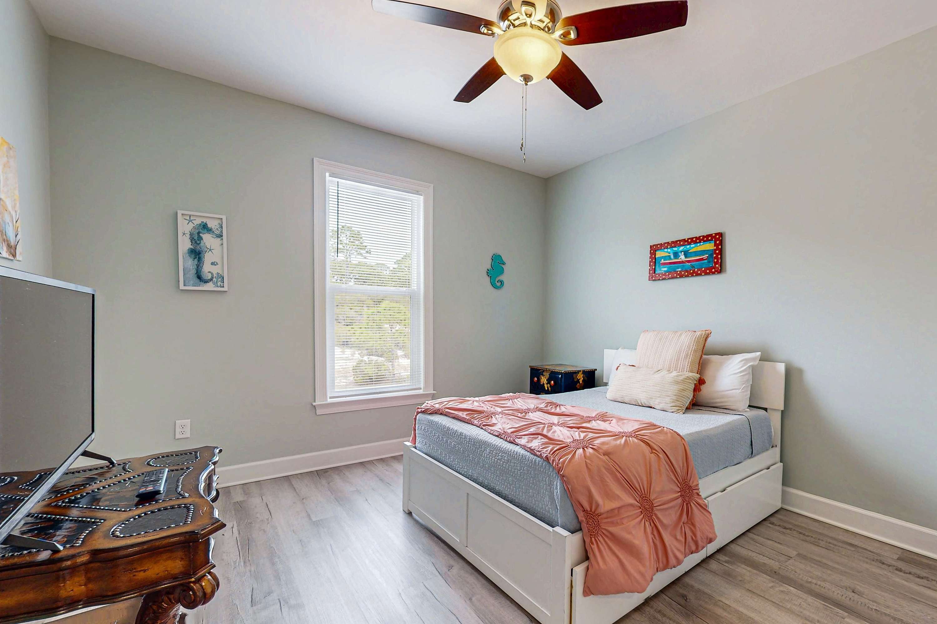 A bedroom with a bed, a ceiling fan, a window, and a dresser.