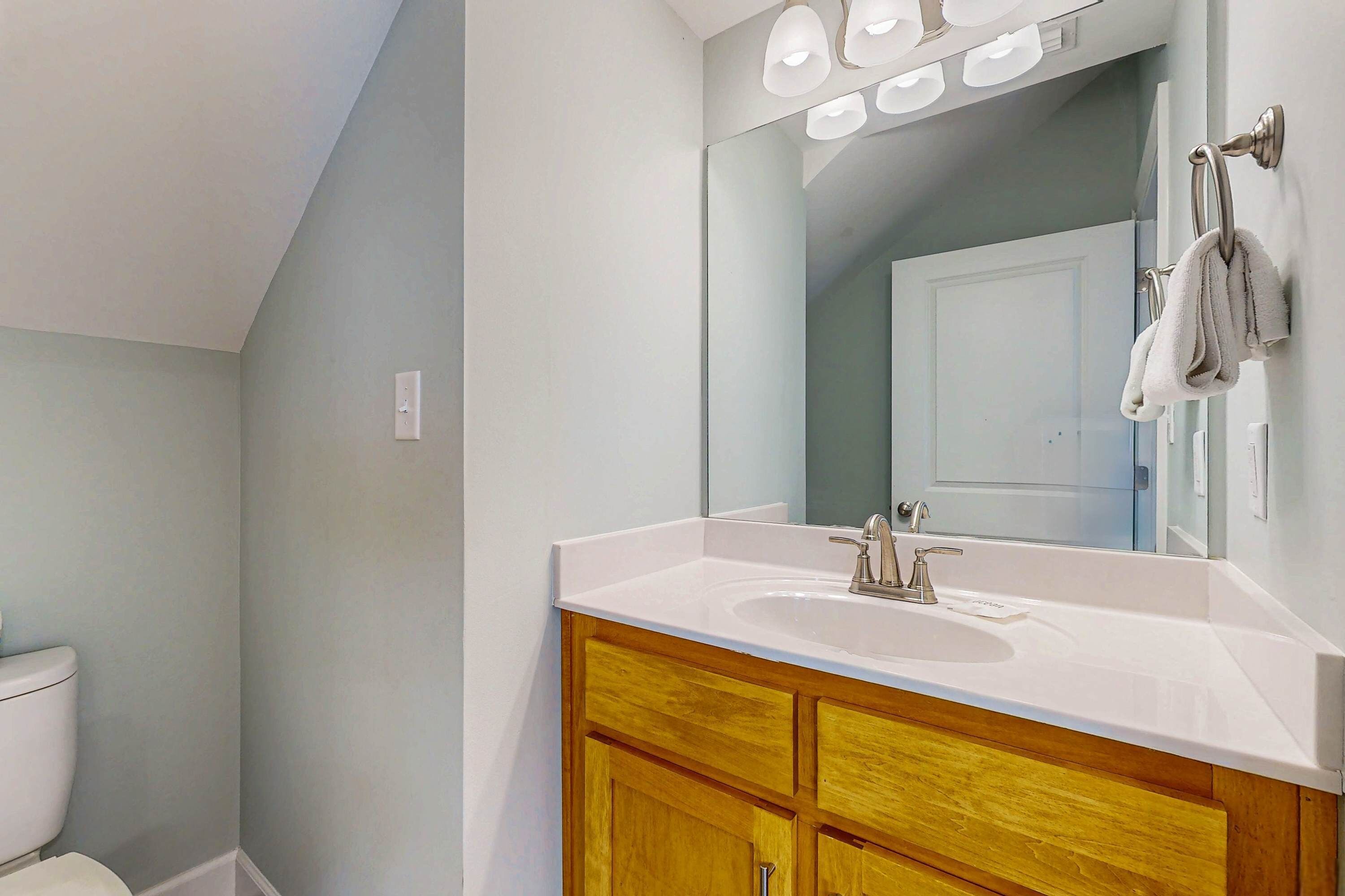 A bathroom with a white sink, wooden vanity, and a mirror above the sink.