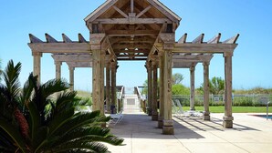 A wooden pavilion with a triangular roof structure, surrounded by palm trees and a clear sky. - Newly renovated second-floor condo with shared pool, WiFi, W/D, & central AC (Dauphin Island)