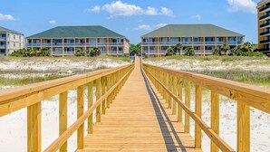 A wooden boardwalk leading to beachfront buildings with balconies and a clear sky. - Newly renovated second-floor condo with shared pool, WiFi, W/D, & central AC (Dauphin Island)