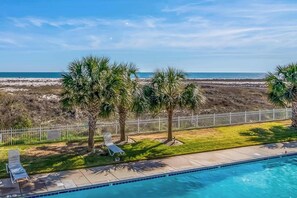Ein Pool mit Blick auf den Strand, Palmen und einem eingezäunten Bereich mit Liegestühlen.