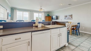 A kitchen with a dishwasher, a sink, a ceiling fan, and a dining area with chairs. - Gulf-Front Condo w/ Balcony, Shared Pools, and Beach Access (Dauphin Island)
