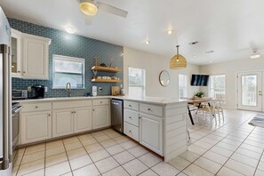 A modern kitchen with white cabinets, a blue-tiled backsplash, and a dining area with a table and chairs. - Spacious private home with patio, balconies, close to beaches (Gulf Shores)