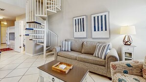 Ein Wohnzimmer mit einem beigefarbenen Sofa, einem Couchtisch, einer weißen Wendeltreppe und gerahmten Kunstwerken an der Wand.