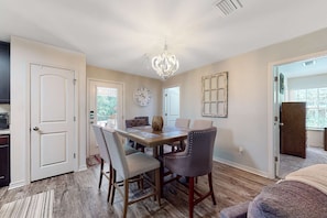 A dining area with a wooden table, chairs, a chandelier, and a clock on the wall. - Seven Rings, Dog-friendly house with back patio, grill, streaming, washer,dryer (Dauphin Island)