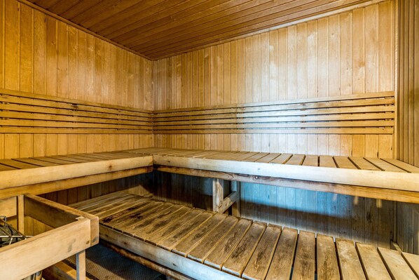 Sauna, jossa on puiset lauteet ja seinät, penkki metallirungolla sekä penkki puurungolla.