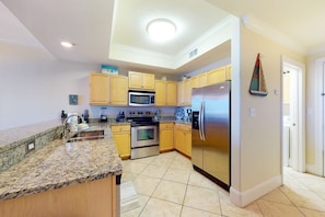 A kitchen with granite countertops, wooden cabinets, stainless steel appliances, and a tiled floor. - Beachfront condo with pool, hot tub, W/D, sauna, balcony, and tennis court (Dauphin Island)