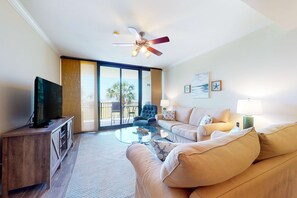 A living room with a television, a sofa, a chair, a coffee table, and a ceiling fan. - Beachfront condo with pool, hot tub, W/D, sauna, balcony, and tennis court (Dauphin Island)