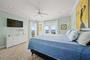Ein Schlafzimmer mit Bett, Deckenventilator, Fernseher, Kommode und Meerblick.