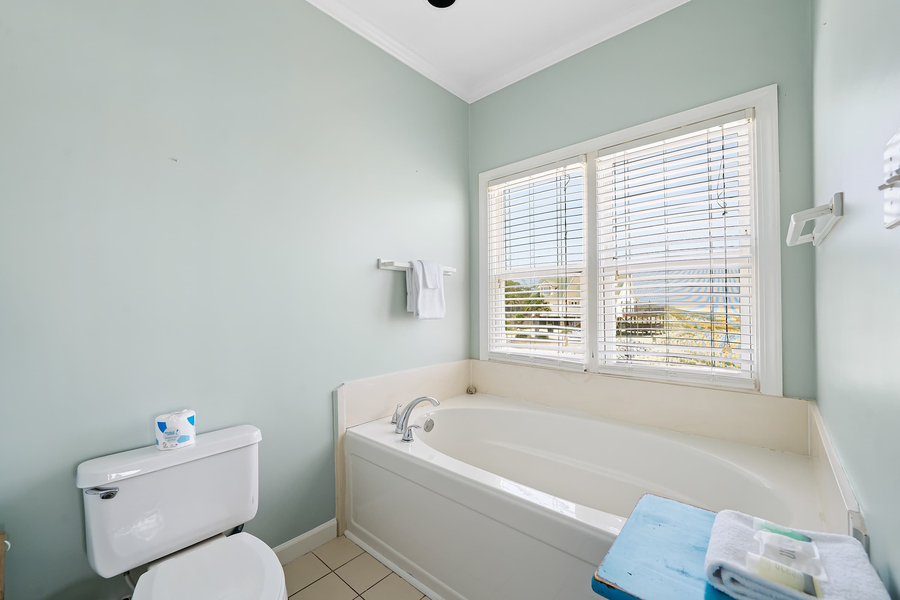 Un baño con inodoro, bañera y ventana con persianas.