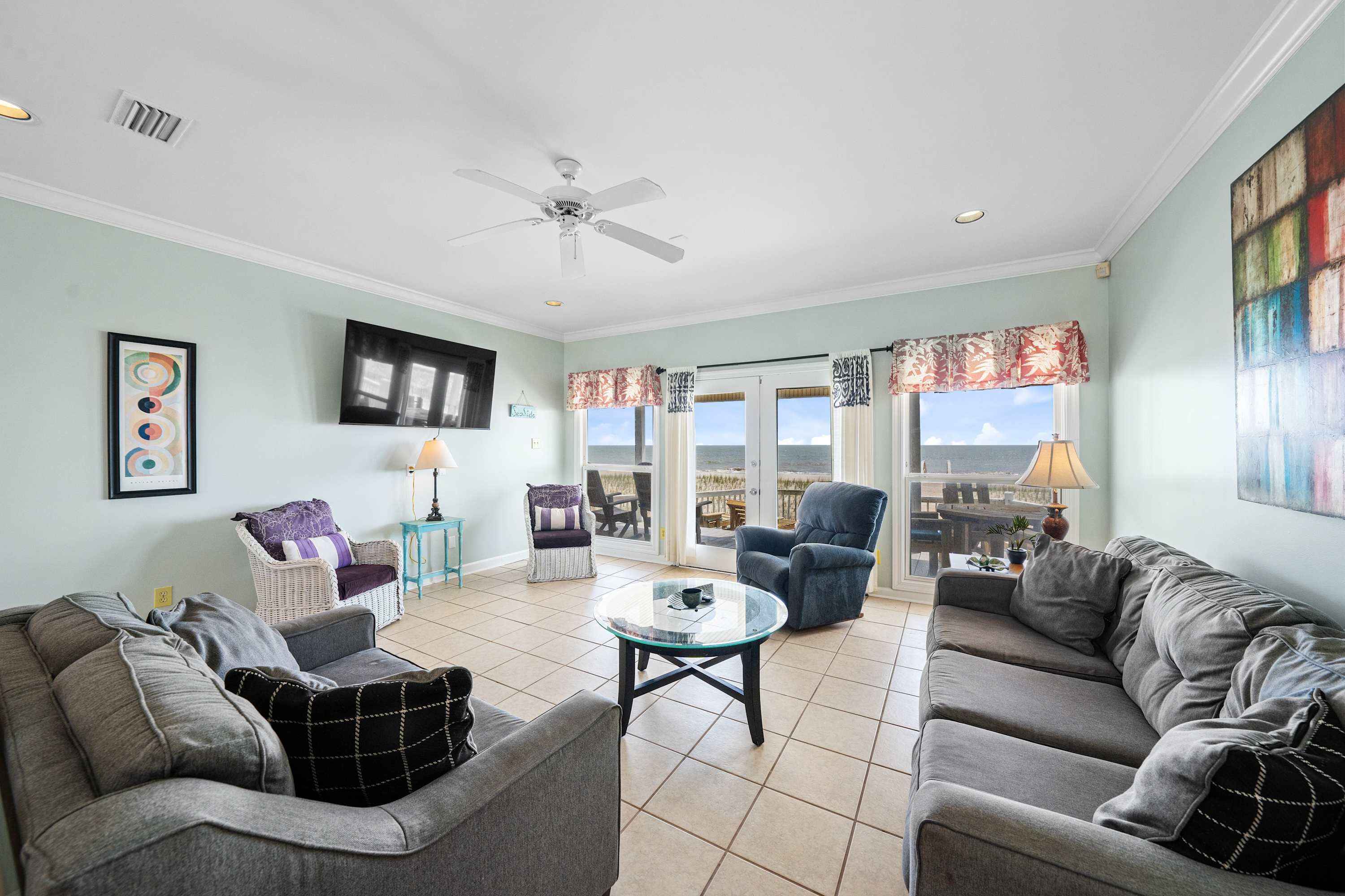 A living room with two sofas, a glass coffee table, a ceiling fan, and a view through a glass door to the outside.