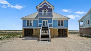 A two-story building with a balcony, a staircase leading to a covered entrance, and a sandy ground. - Gulf front home with private dune walk over, internet, & washer & dryer (Dauphin Island)