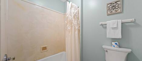 A bathroom with a bathtub, toilet, and shower curtain.