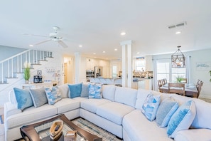 A modern living room with a sectional sofa, a coffee table, and a staircase leading to an upper level. - Bayfront beauty with a pool, grill, dock, reading room, board games, & AC (Dauphin Island)