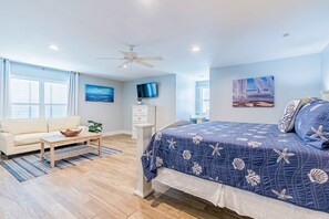 A bedroom with a bed, a sofa, a TV, and a ceiling fan. - Bayfront beauty with a pool, grill, dock, reading room, board games, & AC (Dauphin Island)