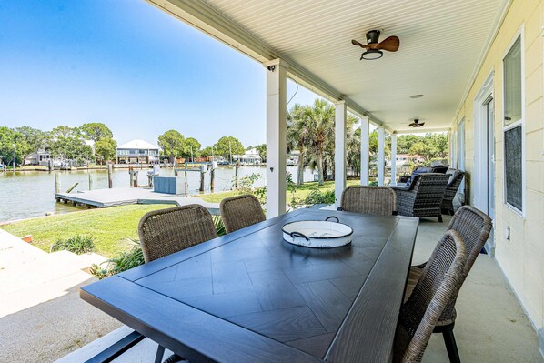 A covered outdoor dining area with a table and chairs, overlooking a body of water and a marina. - Bayfront beauty with a pool, grill, dock, reading room, board games, & AC (Dauphin Island)