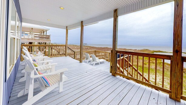 Um deck de madeira com cadeiras e uma mesa brancas, com vista para uma praia.
