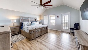 Quarto com cama de madeira, ventoinha no teto, escrivaninha e uma cadeira.