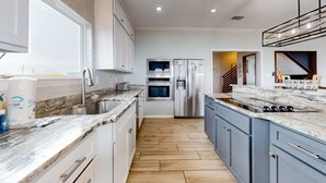 Cozinha moderna com bancada de mármore, eletrodomésticos de aço inoxidável e piso de madeira.
